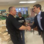 Hampden District Attorney Anthony Gulluni shakes hands with a person as another person watches.