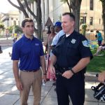Hampden District Attorney Anthony Gulluni talks to a police officer at an outdoor event.