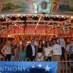 A group of people smile and pose for a photo in front of a carousel.