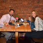 Three people eating at a table smile for a photo.