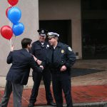 Hampden District Attorney Anthony Gulluni holds balloons and shakes hands with a police officer.