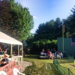 A group of people watch a wiffle ball game.