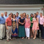 A group of people stand in front of a garage and pose for a photo.