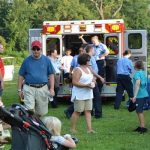 A group of people gathering around an ambulance at an outdoor event.