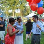 Hampden District Attorney Anthony Gulluni holds balloons and talks to two people at an an outdoor event.