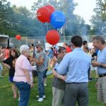 Hampden District Attorney Anthony Gulluni talks to people while holding balloons at an outdoor event.