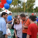 Hampden District Attorney Anthony Gulluni holds balloons and talks to three people at an outdoor event.