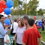 Hampden District Attorney Anthony Gulluni holds balloons and talks to three people at an outdoor event.