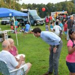 Hampden District Attorney Anthony Gulluni talks to two seated people at an outdoor event,