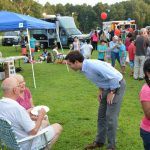 Hampden District Attorney Anthony Gulluni talks with two seated people at an outdoor event.