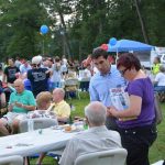 Hampden District Attorney Anthony Gulluni talks to a group of people sitting at a table at an outdoor event.
