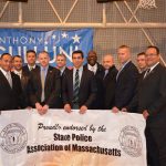 Hampden District Attorney Anthony Gulluni poses for a photo with people in suits as they hold a sign that reads "Proudly endorsed by the state police association of Massachusetts."