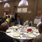 Hampden District Attorney Anthony Gulluni sits at a table with people at an event.
