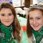 Two girls with green scarves, one wearing a tiara, smile for a photo.