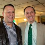A man with a green tie poses for a photo with a man wearing a leather jacket.
