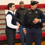 Hampden District Attorney Anthony Gulluni speaks with a police officer in front of red bleachers.
