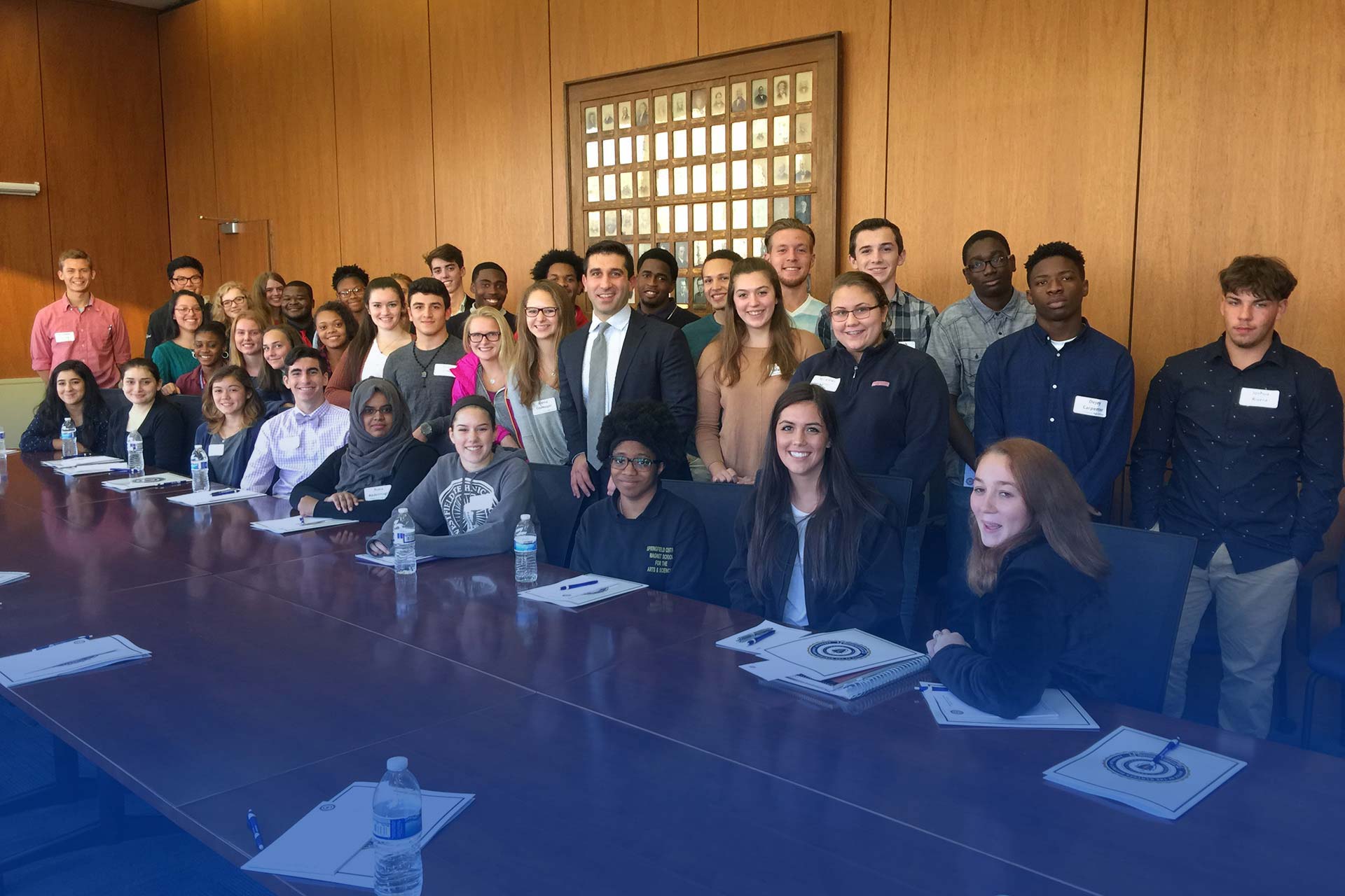 Hampden District Attorney Anthony Gulluni poses for a photo with a group of young adults in a boardroom.