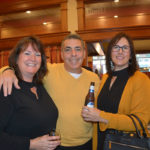 Two women hold drinks and pose with a man for a photo.
